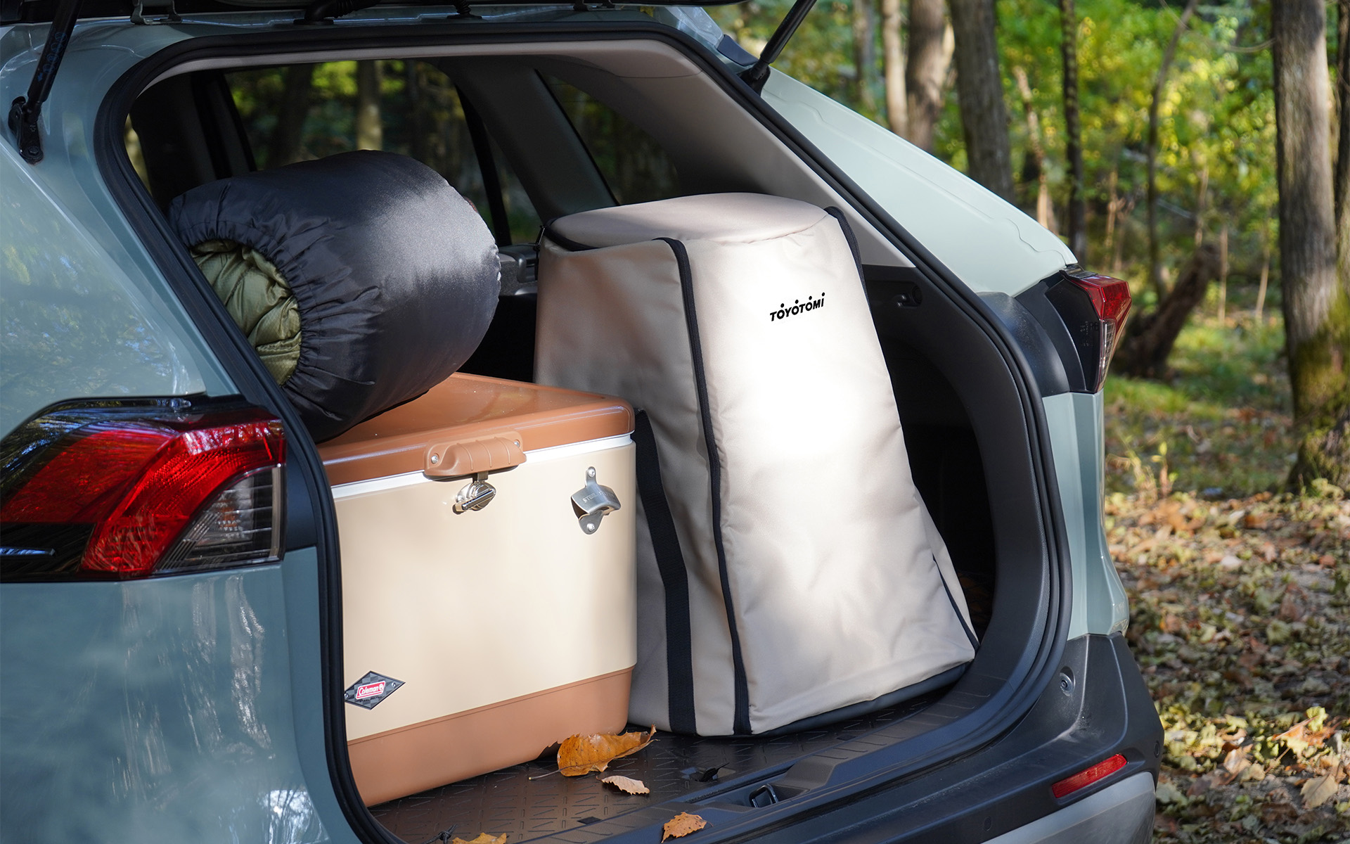 Toyotomi carrying bag in the back of a car next to a cooler and sleeping back, ready for camping
